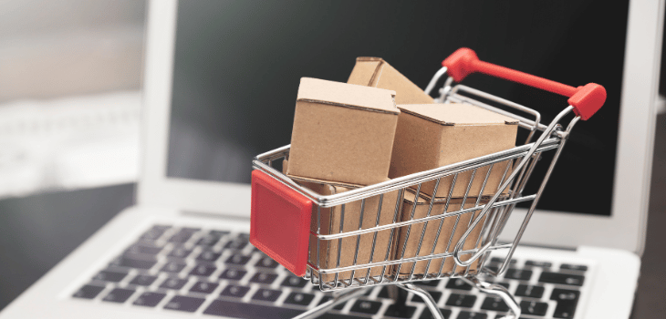 Carrinho de compras, com caixas dentro e encima de um notebook