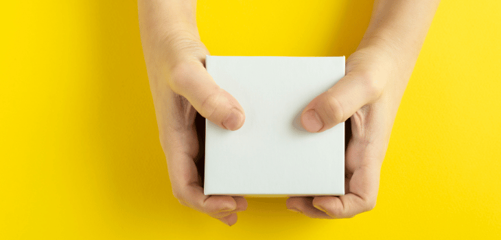 Mãos brancas segurando uma embalagem minimalista branca em um fundo amarelo.